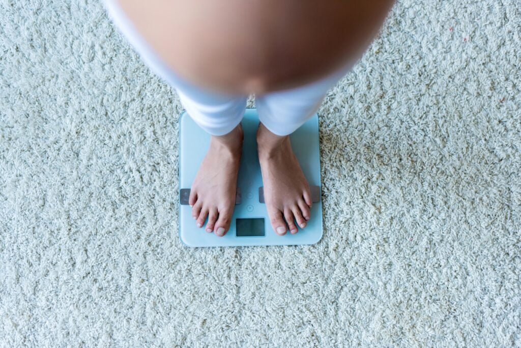 Cropped shot of legs of pregnant woman standing on scales.